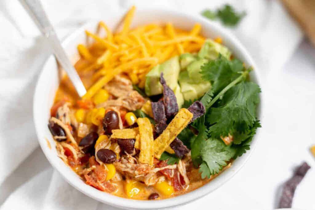 Chicken taco soup topped with shredded cheese, corn chips, and cilantro.