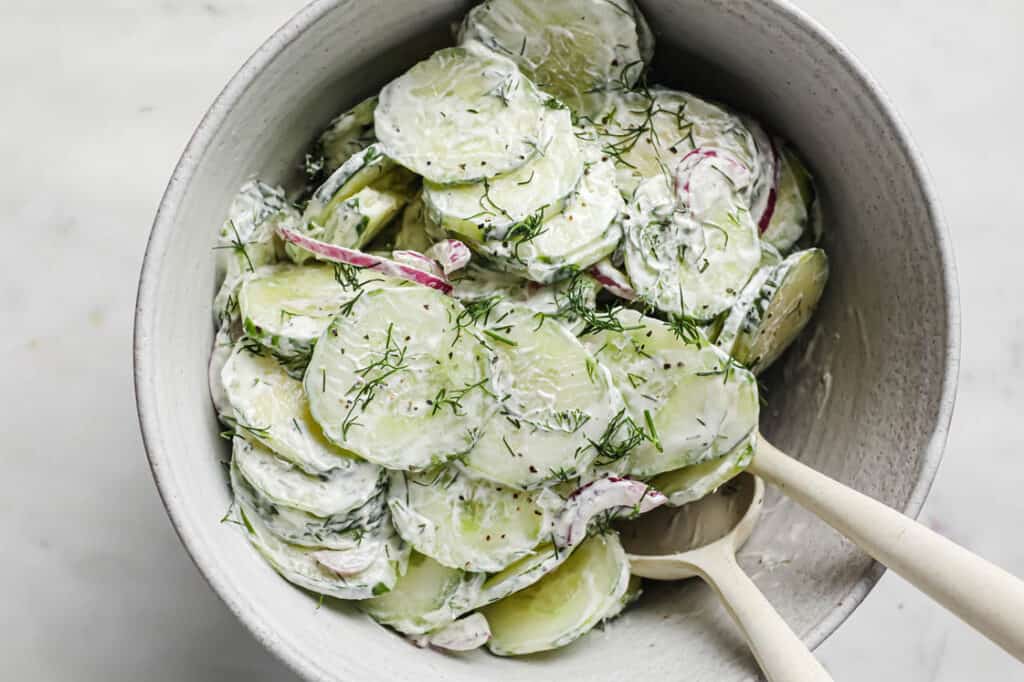 Bowl of creamy dill cucumber onion salad in a bowl with spoons.