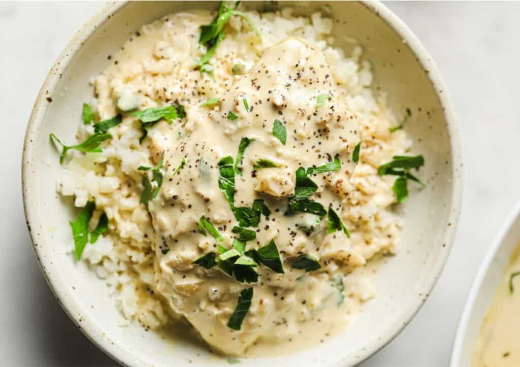 Garnished creamy garlic chicken over cauliflower rice in a bowl.
