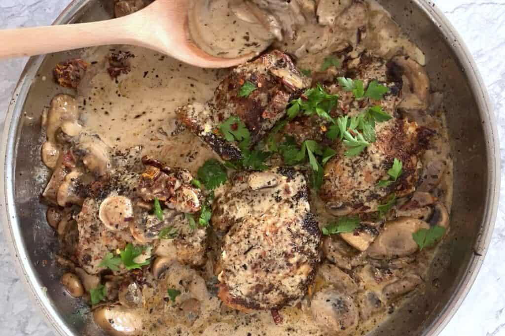 Pan of creamy mushroom sauce chicken thighs garnished with parsley.