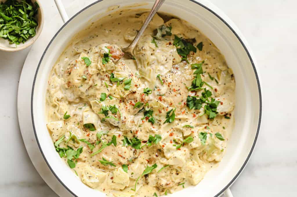 Creamy chicken thighs with artichoke hearts in a pan.