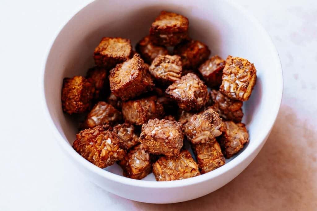 A small white ceramic bowl filled with cooked, cubed tempeh.