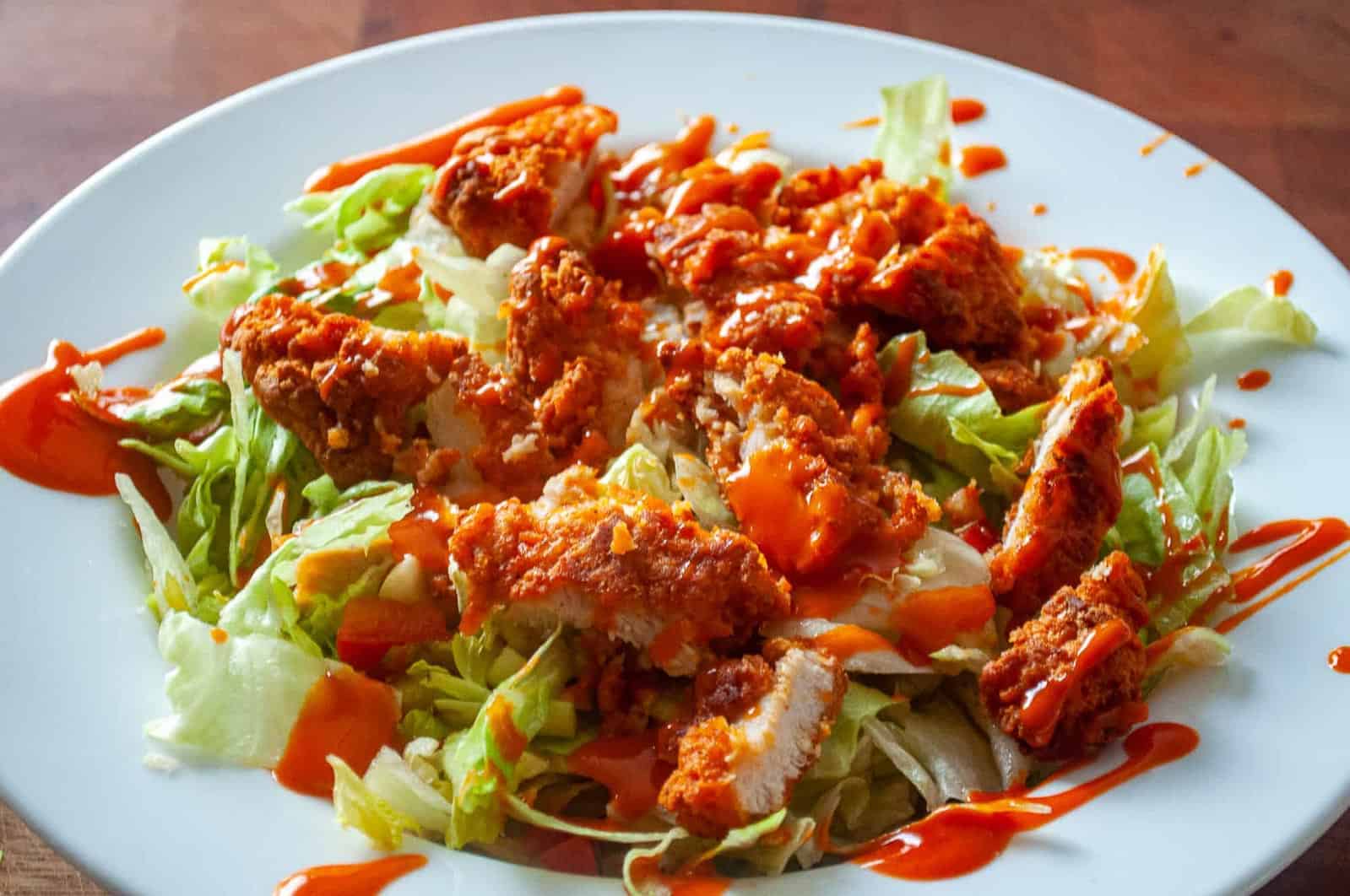 A crispy buffalo chicken salad featuring crispy chicken, buffalo sauce, blue cheese, and dressing.