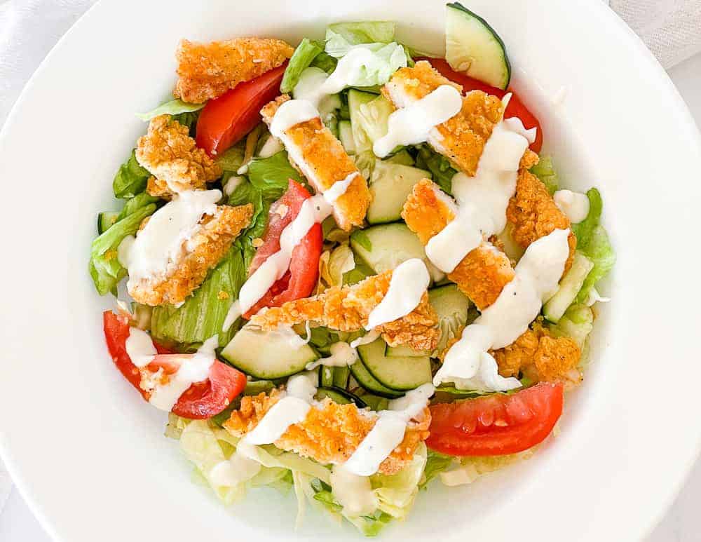 A salad with crispy chicken and dressing on top.
