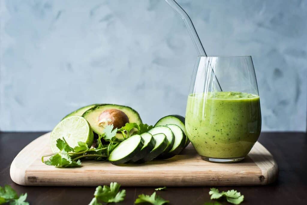 A cucumber avocado smoothie on a cutting board next to the ingredients.