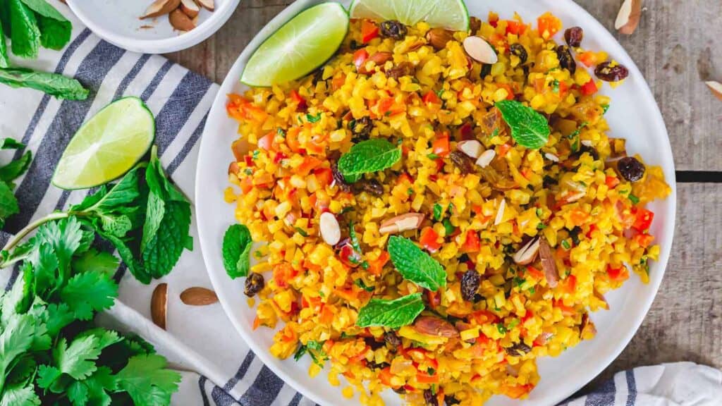 Curry cauliflower rice on a white plate garnished with mint and lime wedges.