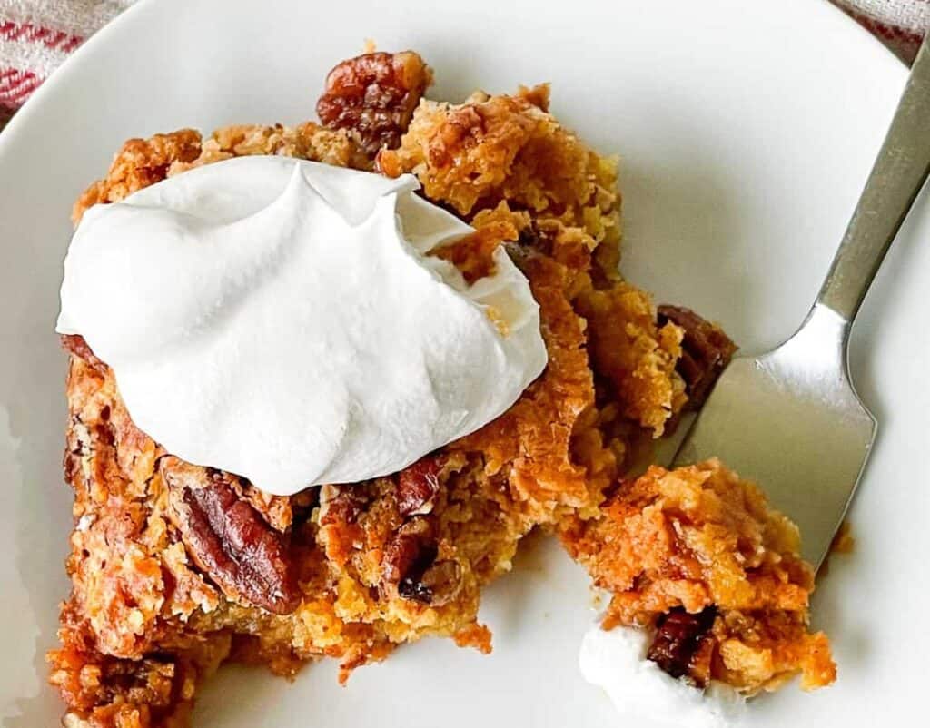 Pumpkin Crunch Cake on a plate with a fork and dollop of whipped cream.