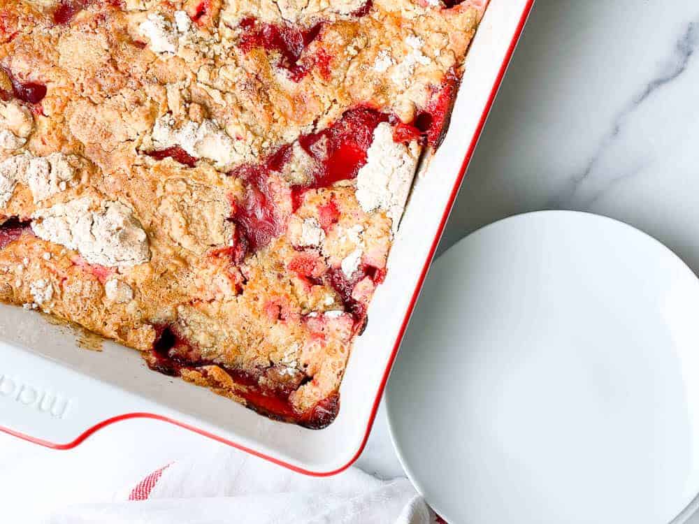 Strawberry dump cake in a baking dish with plates next to it. 