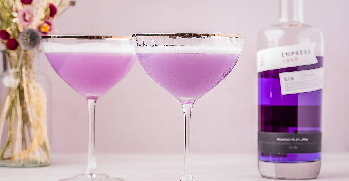 Two empress 1908 gin sours next to a bottle of purple gin.