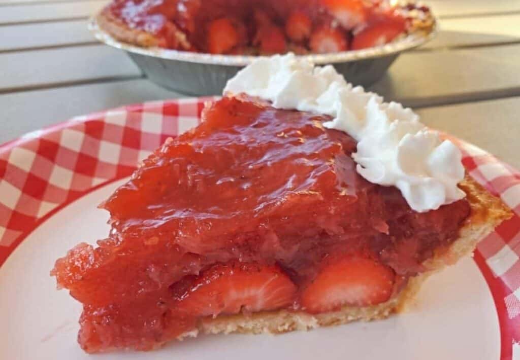 Slice of strawberry pie on a plate with the whole pie in the background.