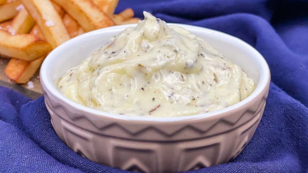 Garlic dip in a serving bowl with fries by it.