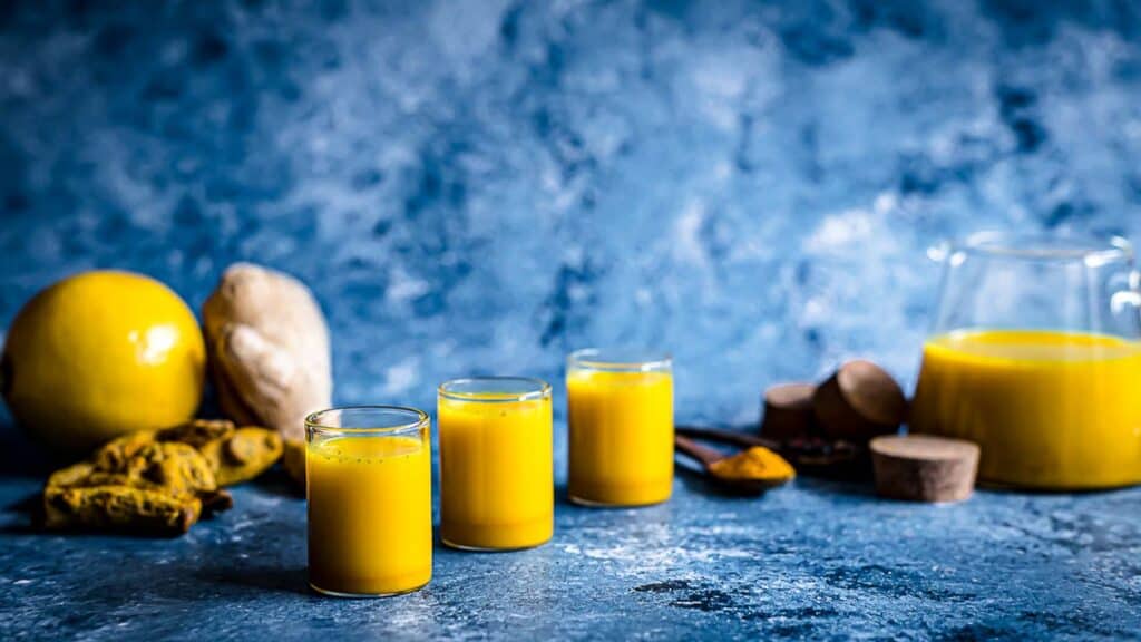 Ginger Turmeric Shots on a blue board with jug behind. 