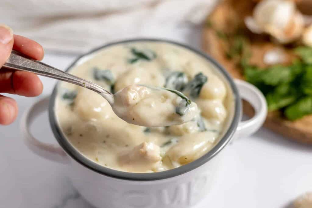 Chicken and Gnocchi Soup in a spoon over a bowl of soup.