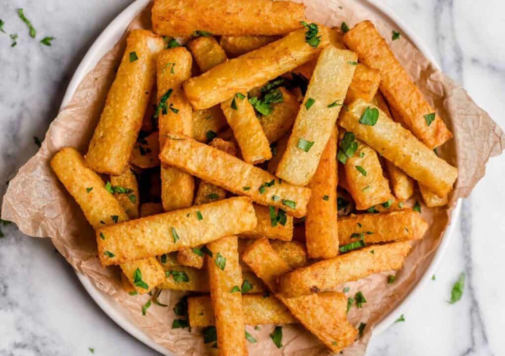 Golden baked jicama fries garnished with parsley on a plate.