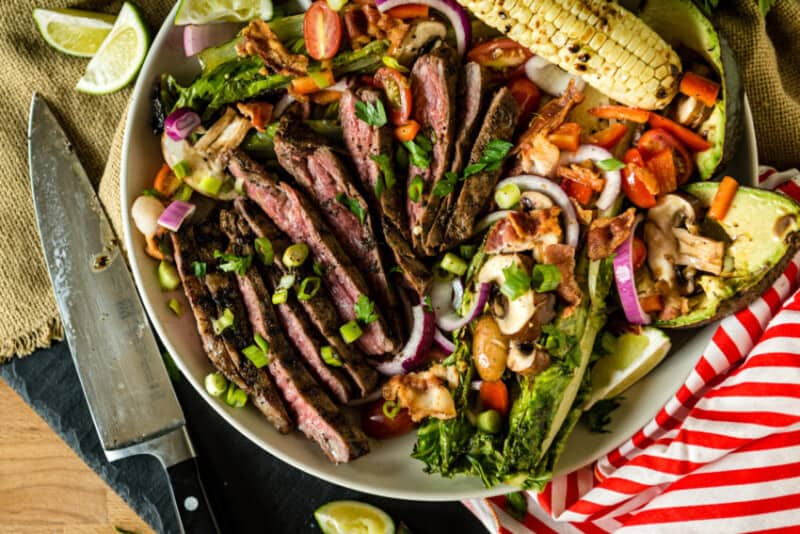 Overhead shot of beautifully grilled flank steak over colourful salad.