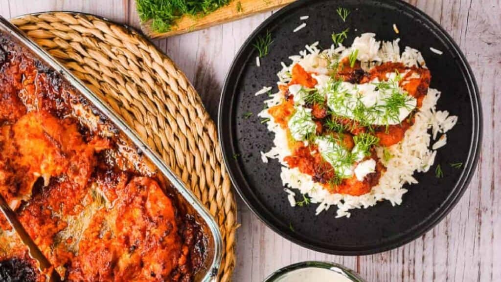 Harissa chicken on a black plate with rice and dill.