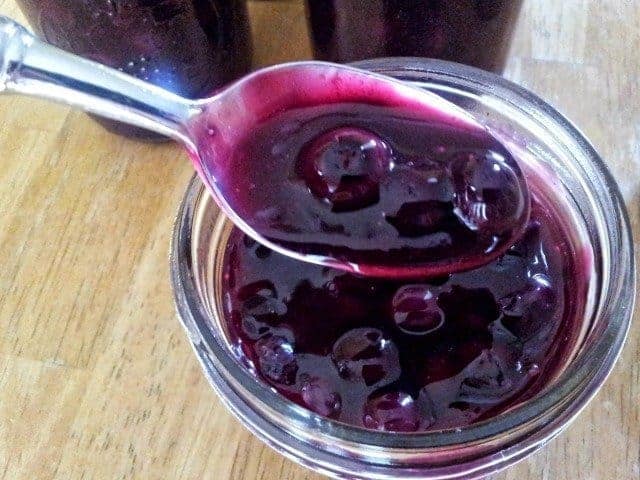Overhead shot of a spoon containing blueberry syrup being held over a jar with more syrup.
