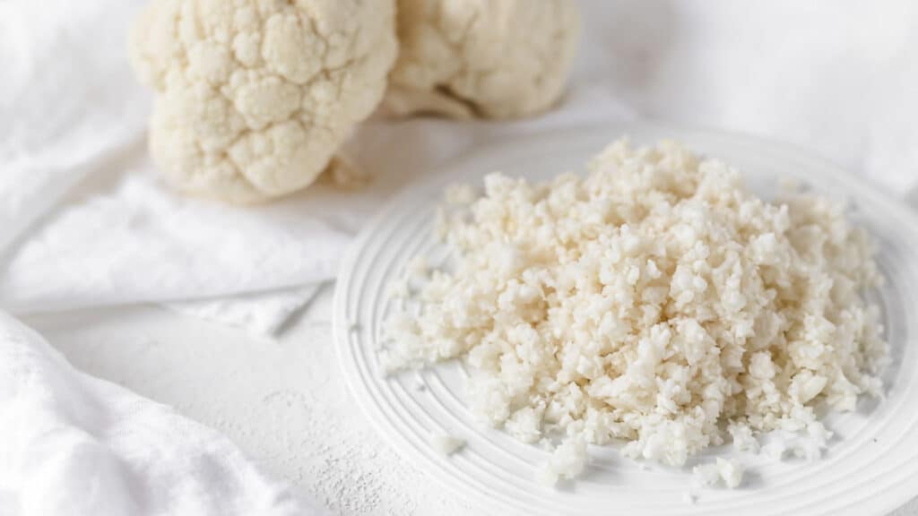 Cauliflower Rice on a white plate with whole cauliflower on the side. 