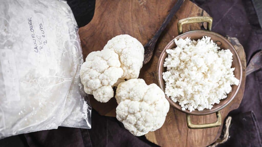 Cauli rice in a golden bowl with cauliflower head on the side.