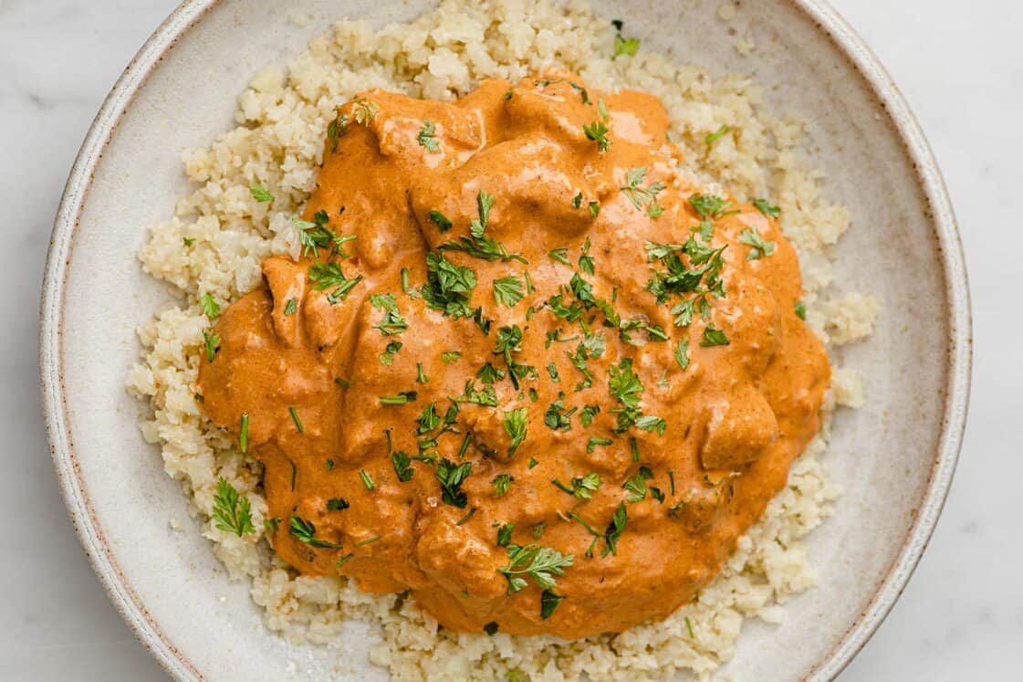 Bowl of instant pot butter chicken atop cauliflower rice in a bowl.