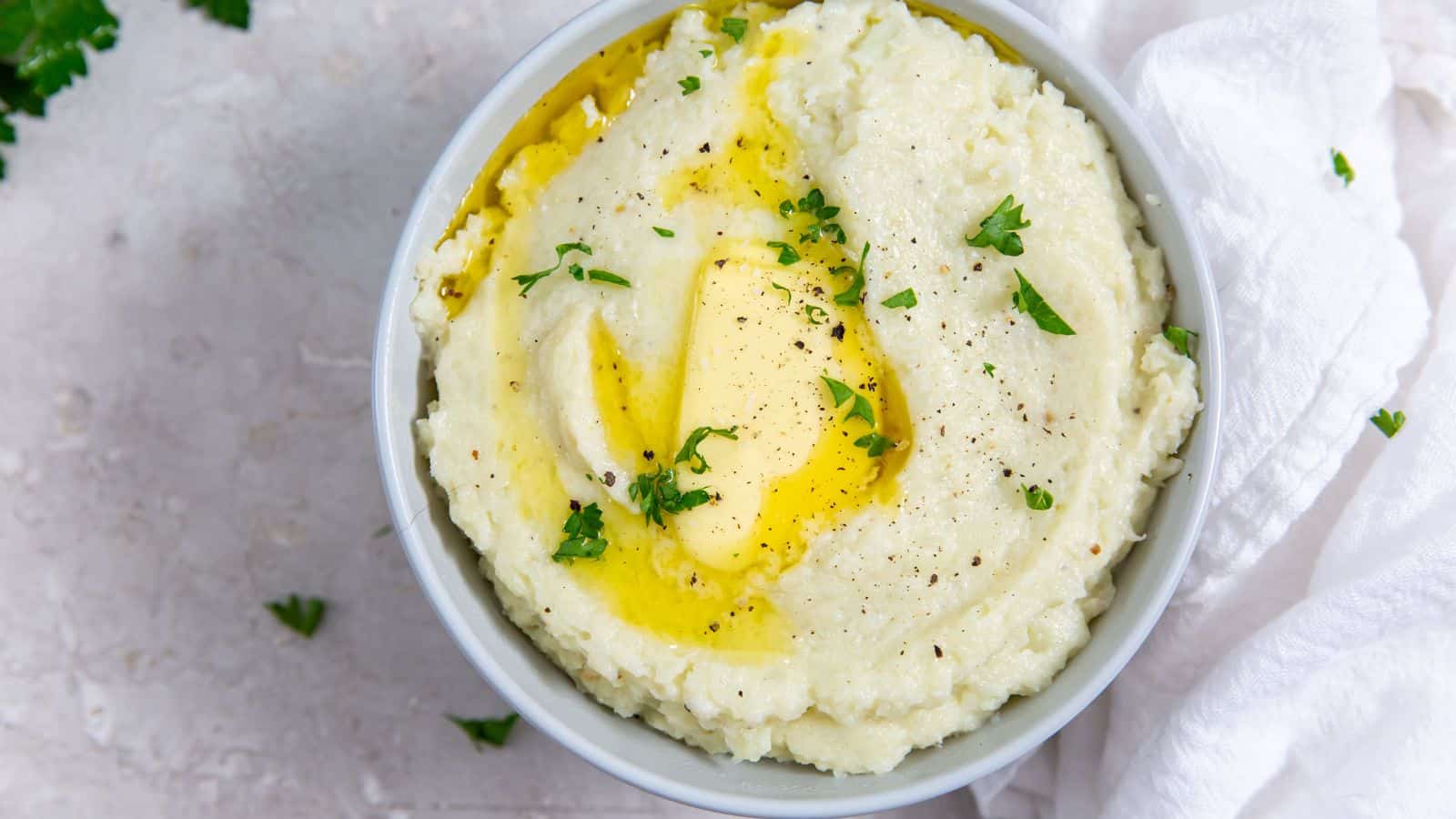 Instant Pot Mashed Cauliflower in a white bowl with a spoon, parsley, butter, salt, and black pepper.