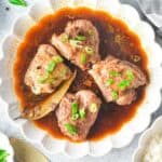 Chicken adobo in a white bowl with rice and scallions on the side.