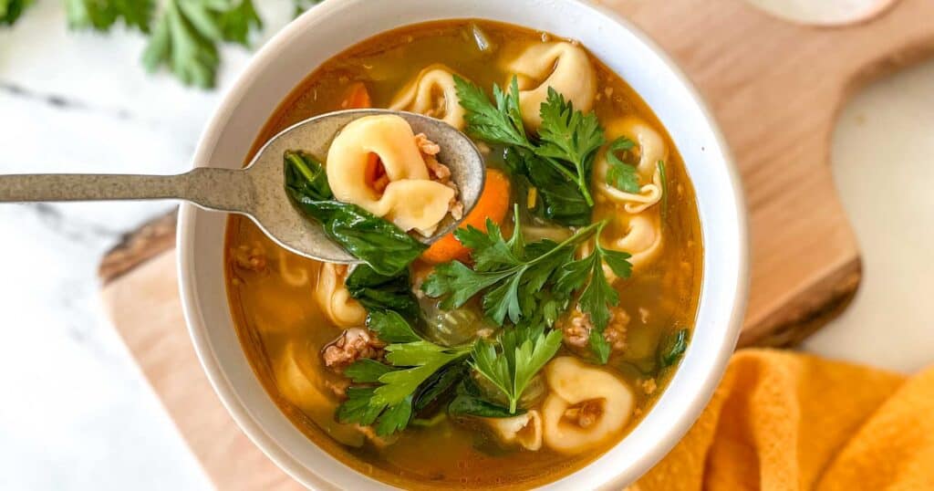 a bowl of instant pot tortellini soup on a wooden cutting board.
