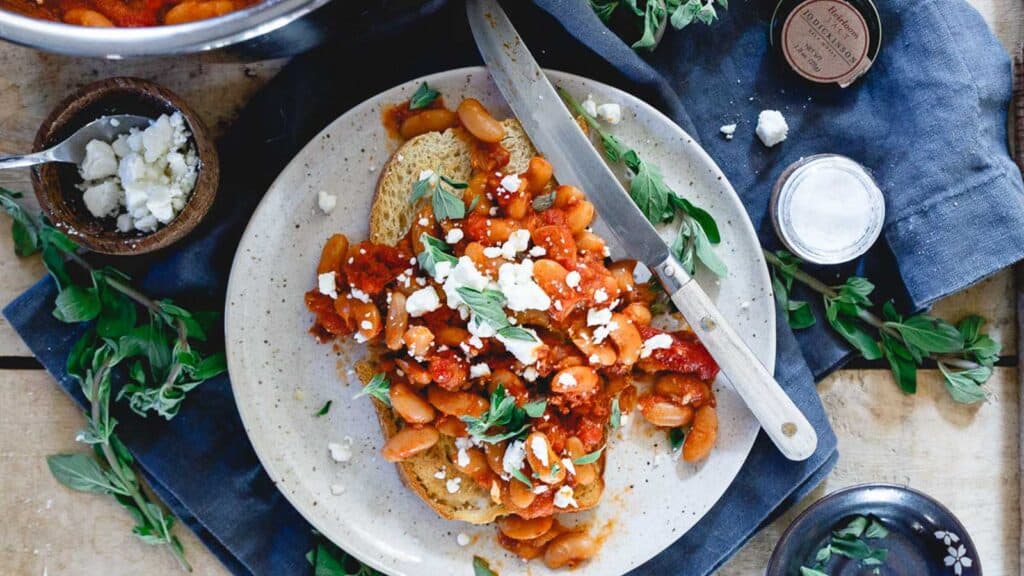 Instant Pot white beans and tomatoes on sourdough toast garnished with fresh herbs and crumbled feta.