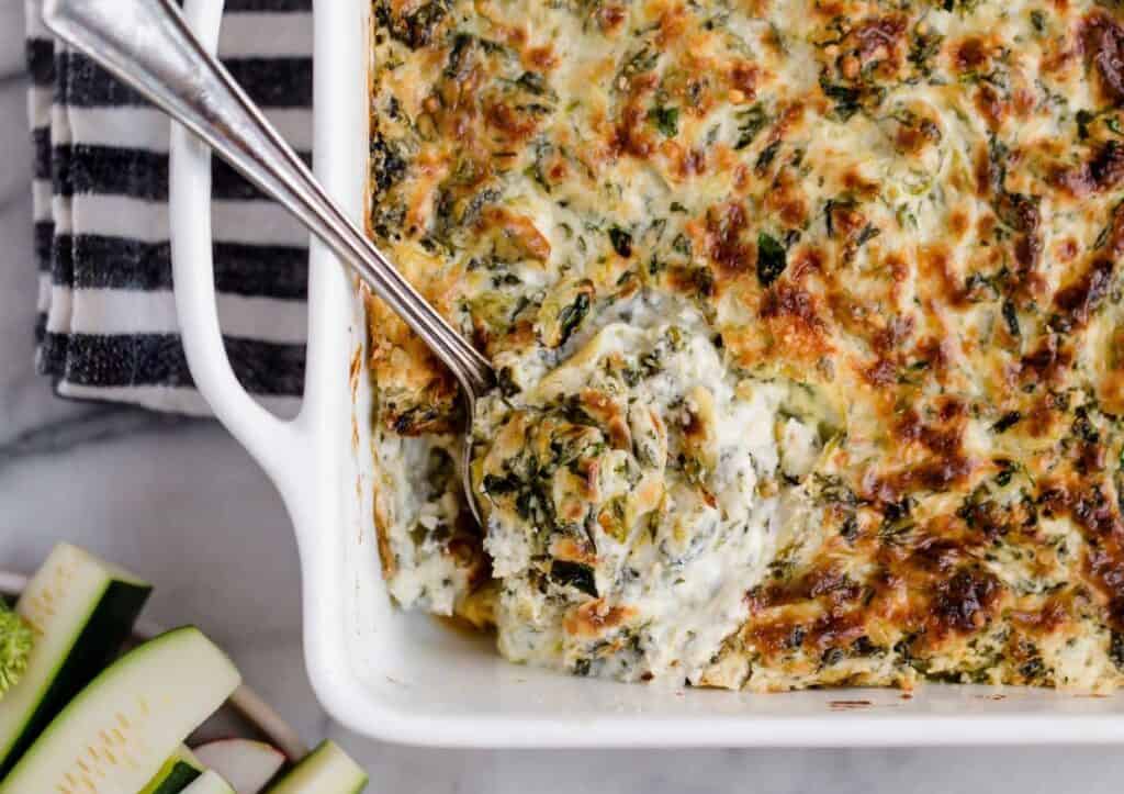 A dish of jalapeño spinach artichoke dip with a spoon scooping out a serving.