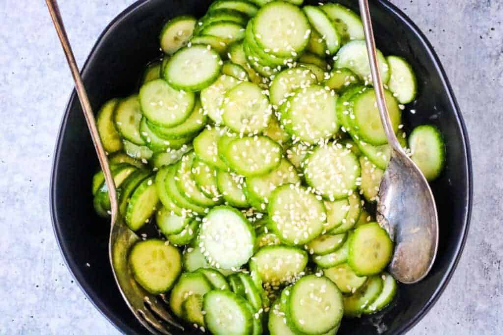 A black bowl of Japanese cucumber salad garnished with sesame seeds.