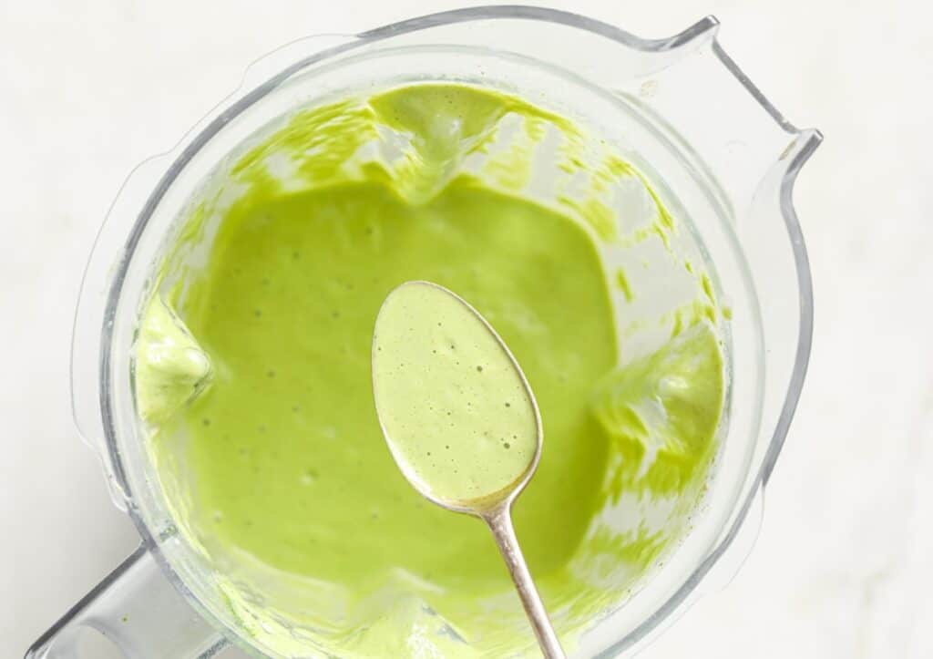 A spoon of keto green smoothie atop a blender.