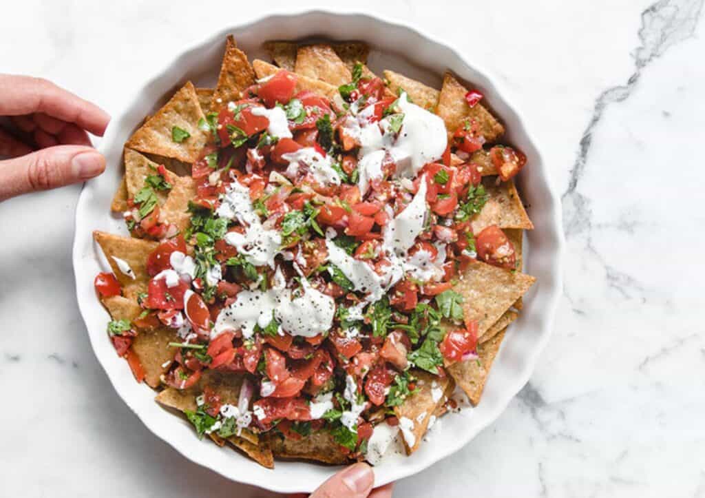 Two hands holding a plate of keto nachos.