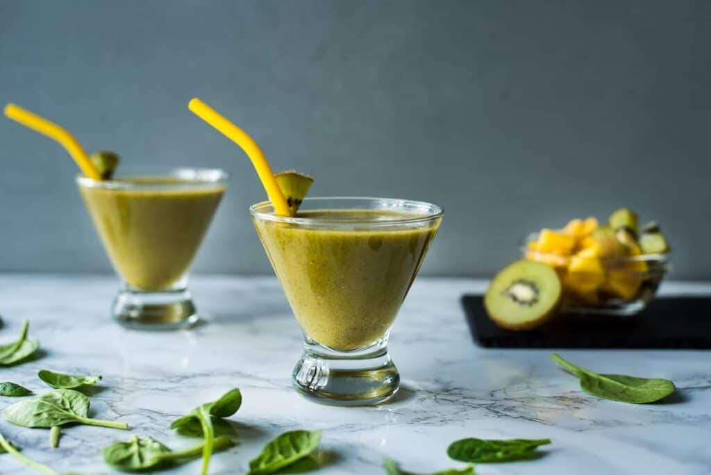 Two kiwi mango smoothies in glasses with straws.