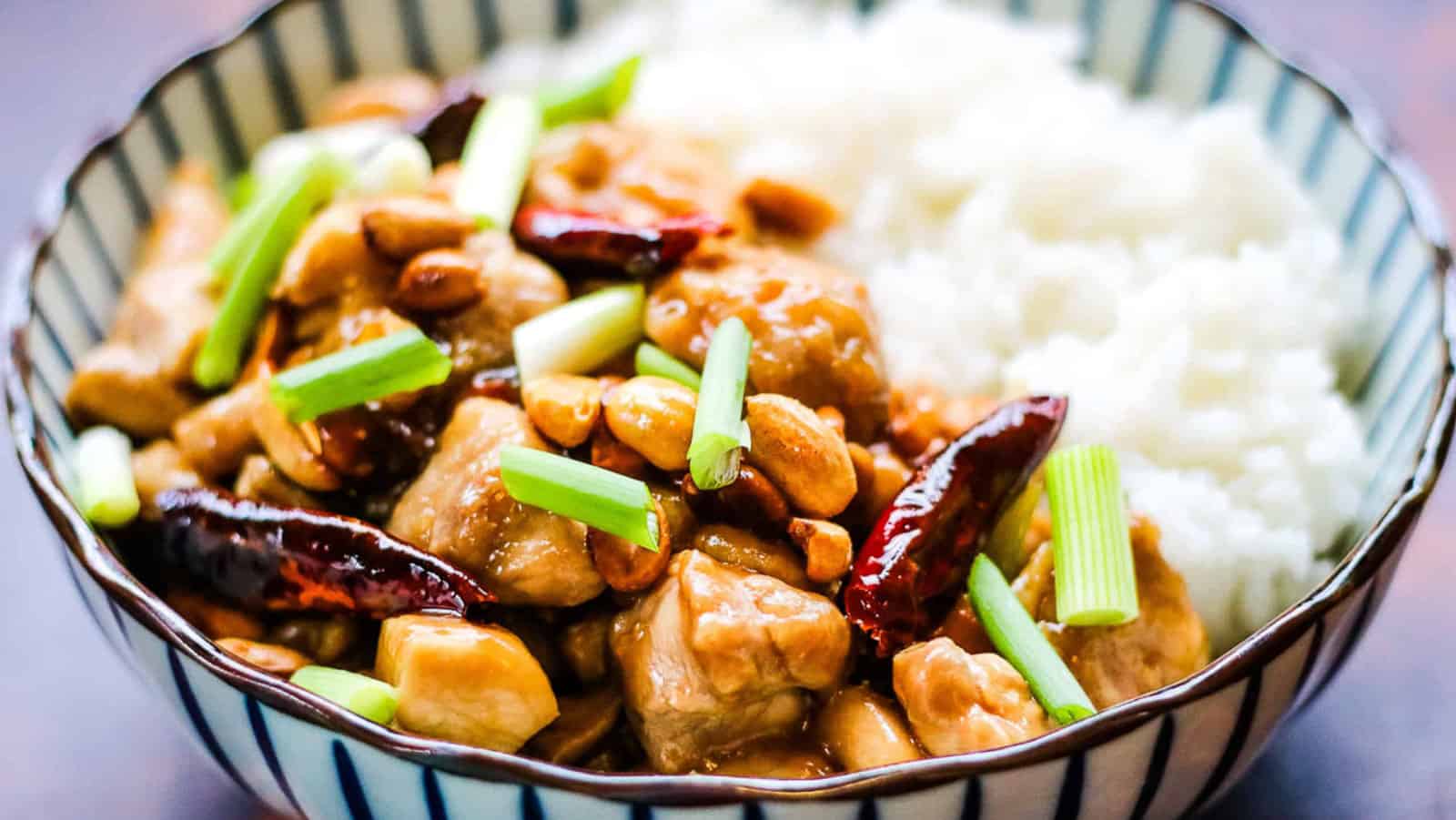 Kung pao chicken in a striped bowl with rice.