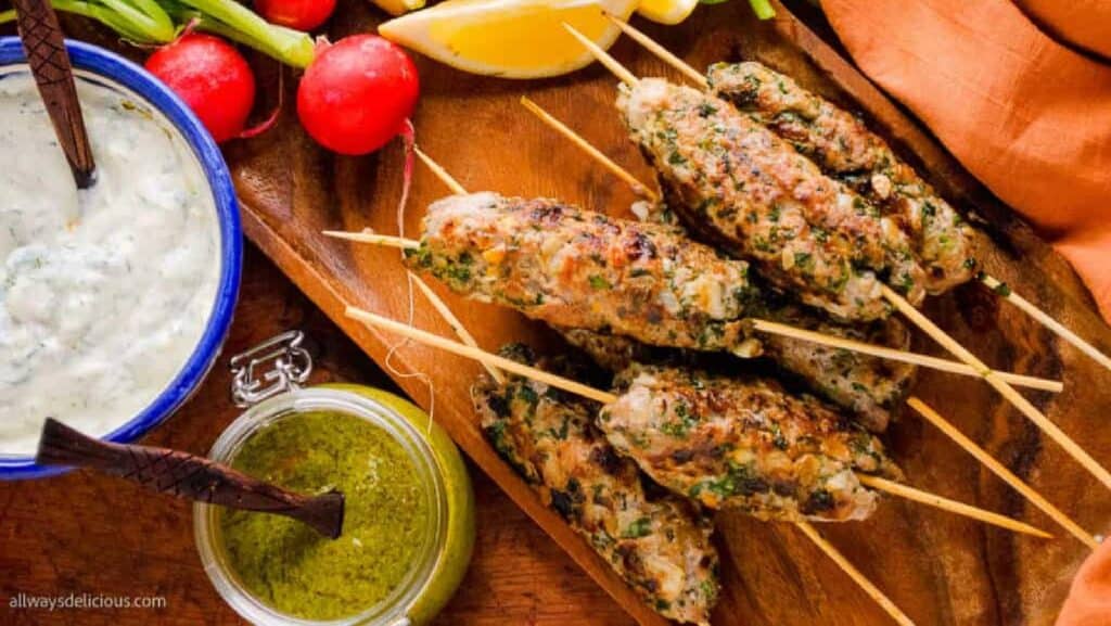 Lamb kofta kebabs on a wooden tray with vegies and sauces.