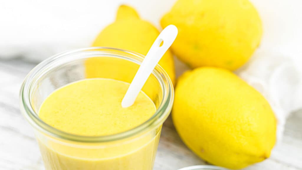 Keto Lemon Curd inide a glass with fresh lemons behind. 