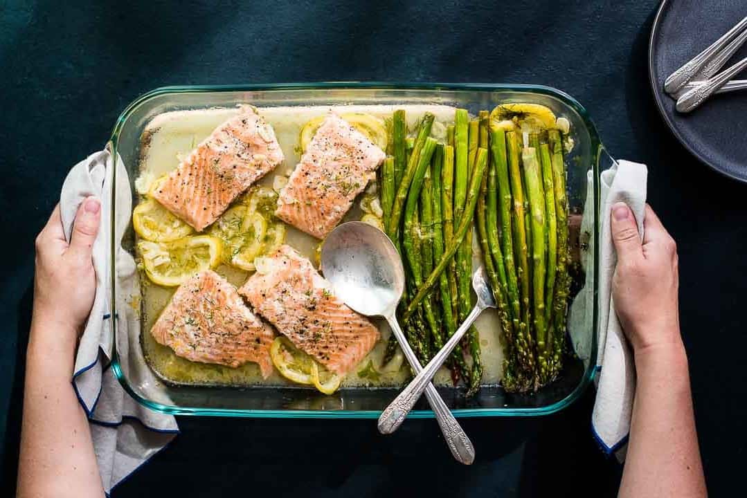 Hands holding a baking dish with Lemon Dill Salmon and Asparagus.