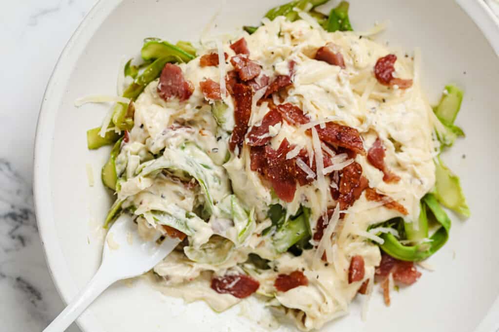 Bowl of creamy bacon asparagus pasta with a fork.