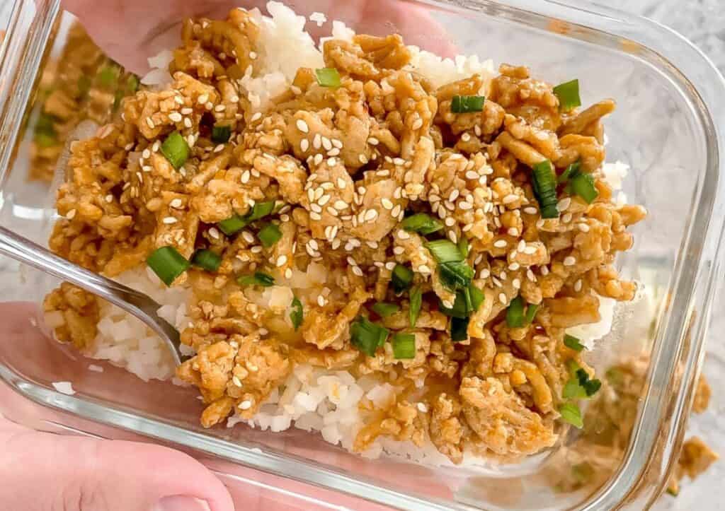 Meal prep firecracker ground chicken garnished with green onions in a glass container.