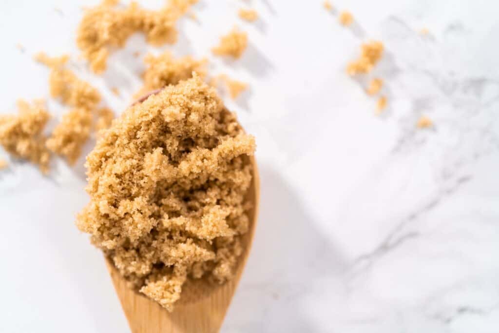 Overhead shot of brown sugar piled on a wooden spoon with a marble counter in the background.
