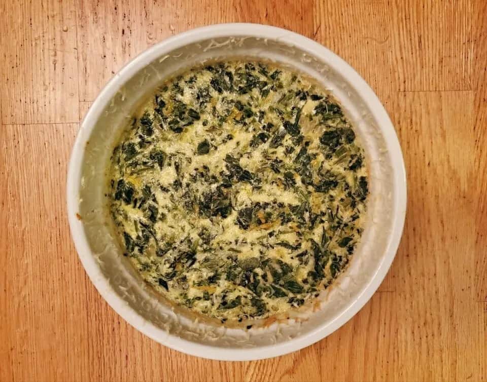 This photo shows and overhead shot of a spinach souffle in a round white casserole dish.