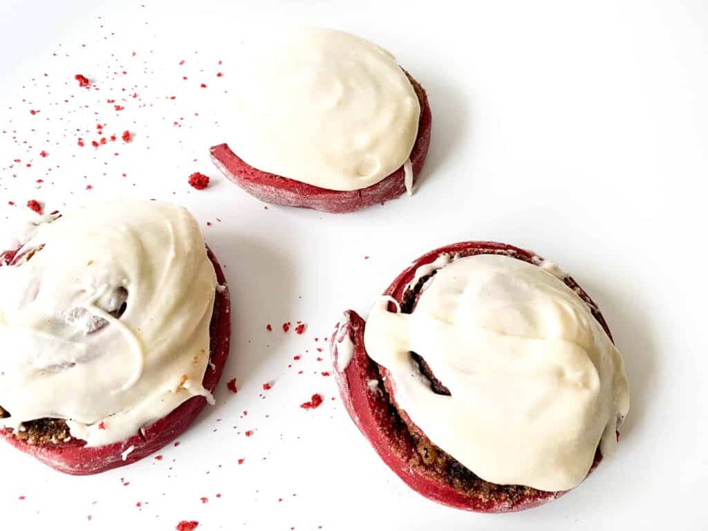Red Velvet Cinnamon Rolls on a white counter tops with crumbs around them too.