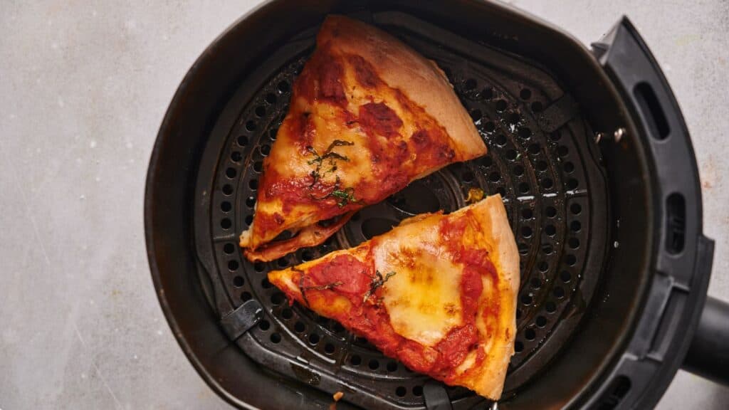 Two slices of pizza in an air fryer basket.