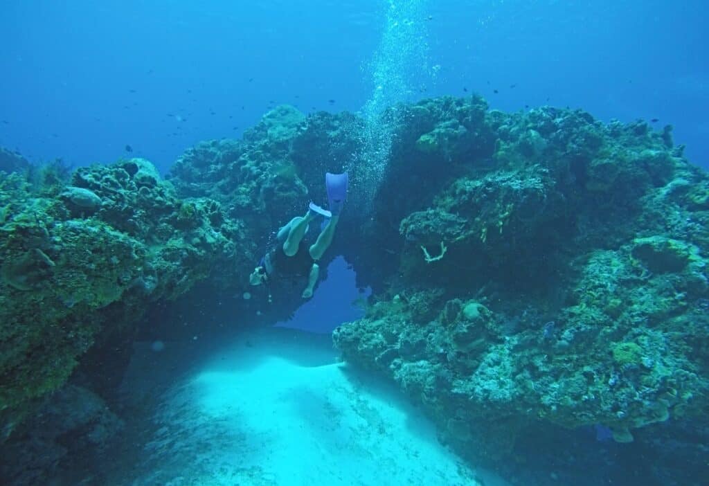 View from behind of a SCUBA diver about to swim through a hole in a reef with bubbles escaping to the surface.