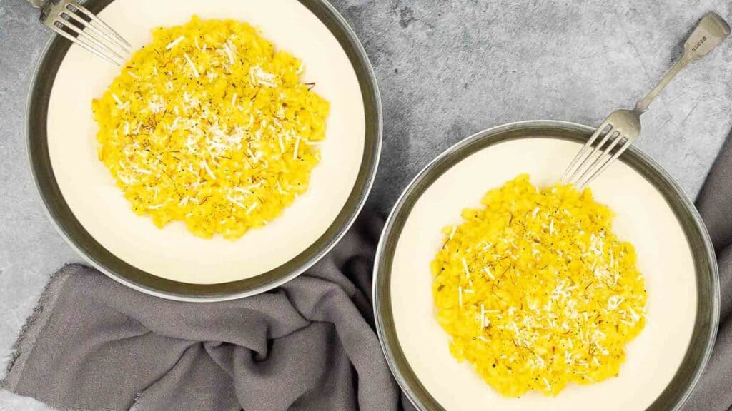 Two dishes of saffron risotto with forks on the side.