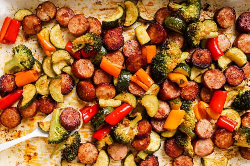 Sausage and veggies sheet pan dinner with a spoon.