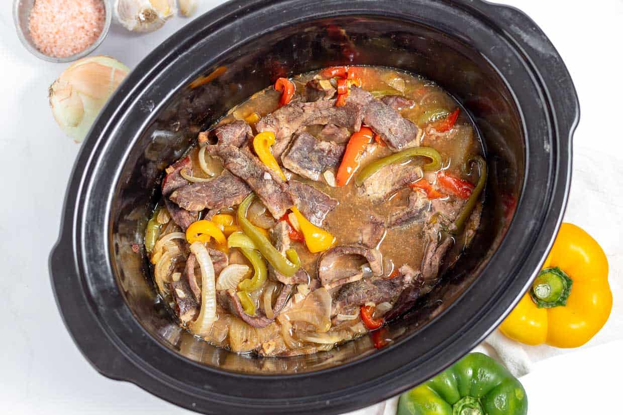 A crock pot filled with beef and peppers.