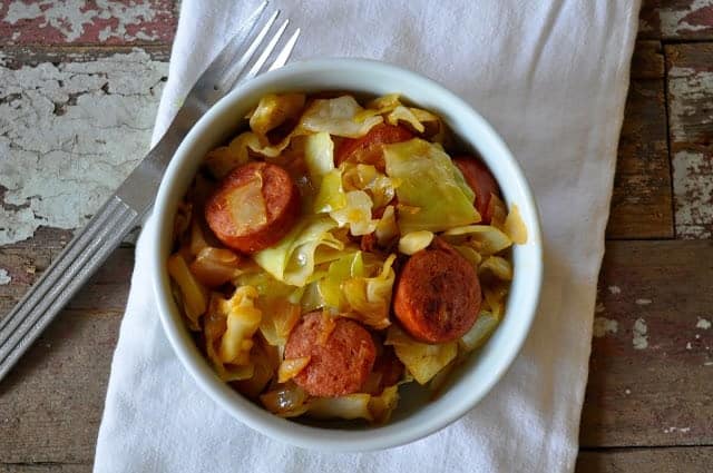 Cabbage and smoked sausages in a bowl with a fork. 