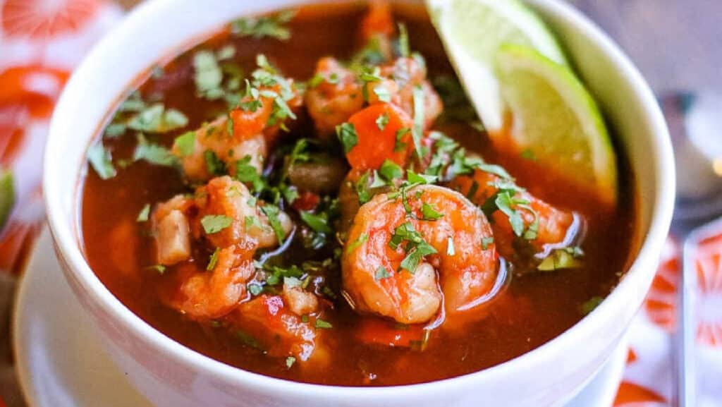 Shrimp soup in a white bowl with lime wedges.