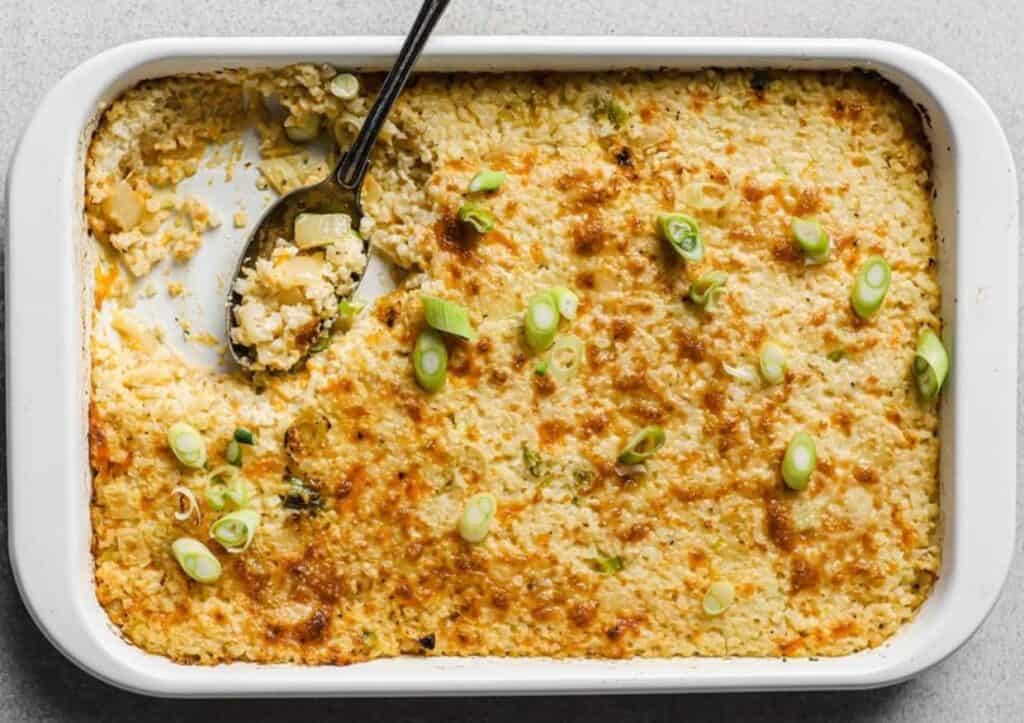 Sour cream and onion cauliflower bake in a baking dish with a spoon.
